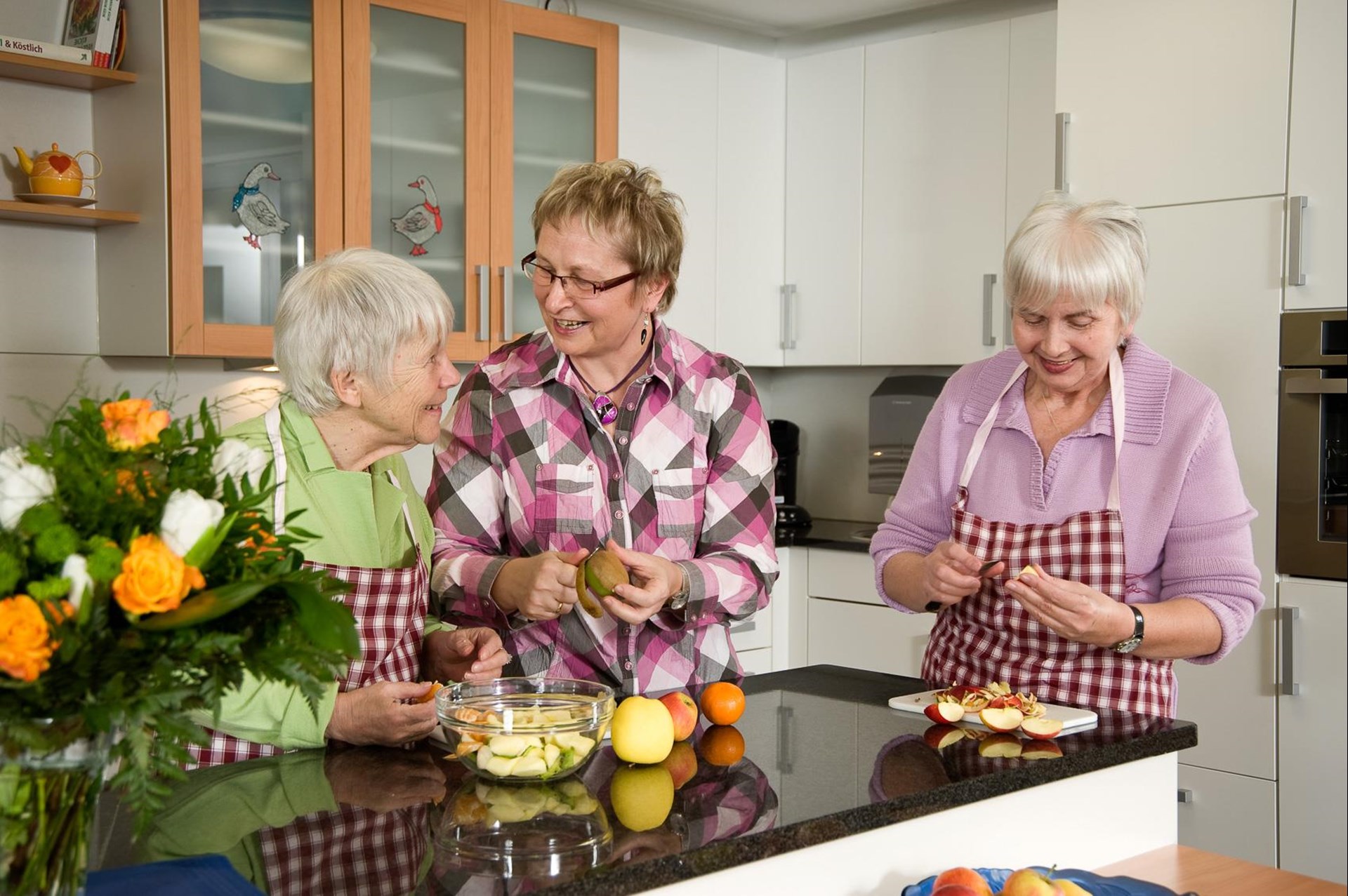 Bewohnerinnen bereiten mit einer Betreuerin das Essen vor